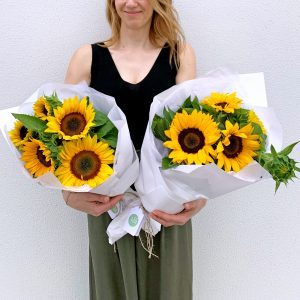 Florist holding two cheerful sunflower bouquets wrapped in white paper.