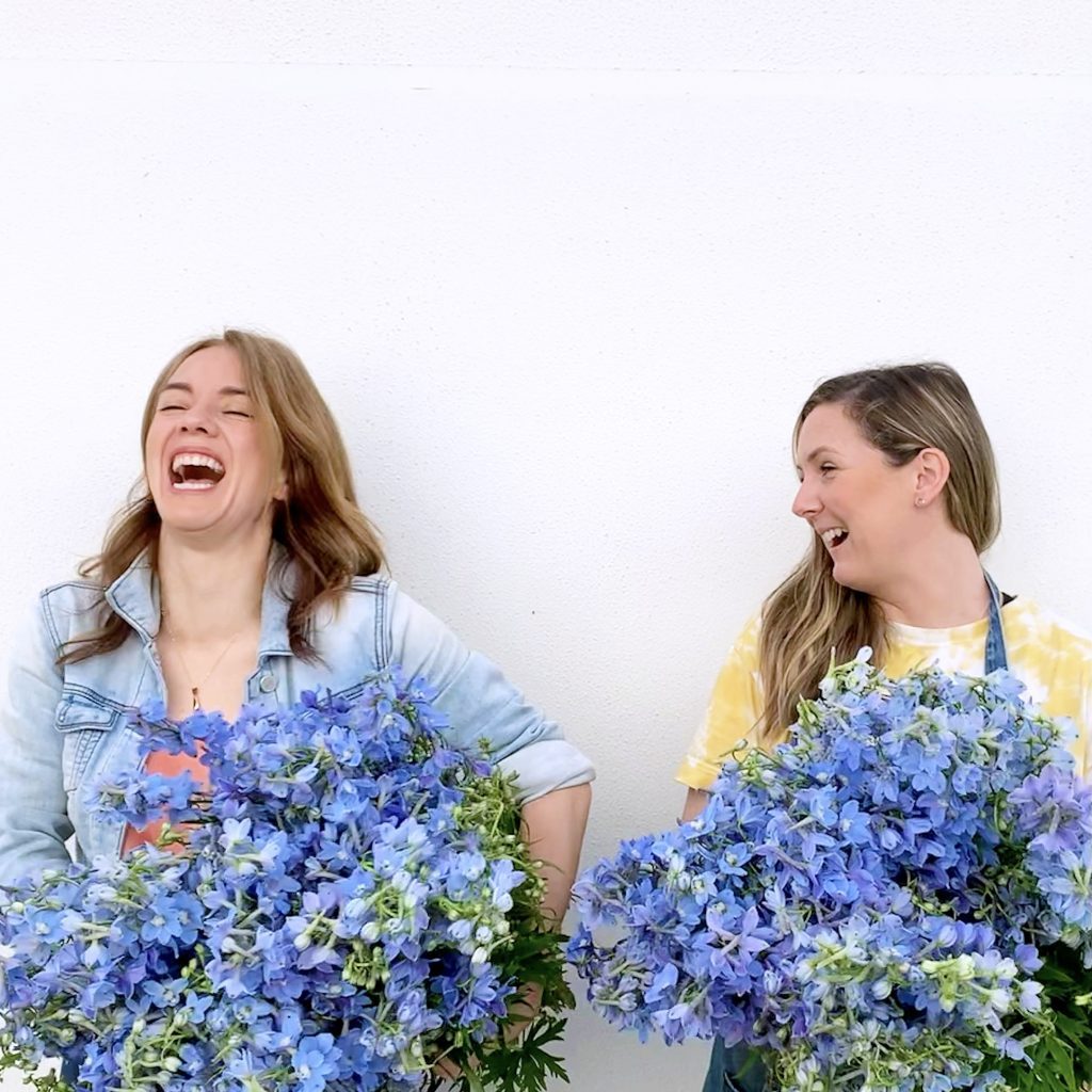 Two friends laughing withblue delphiniums