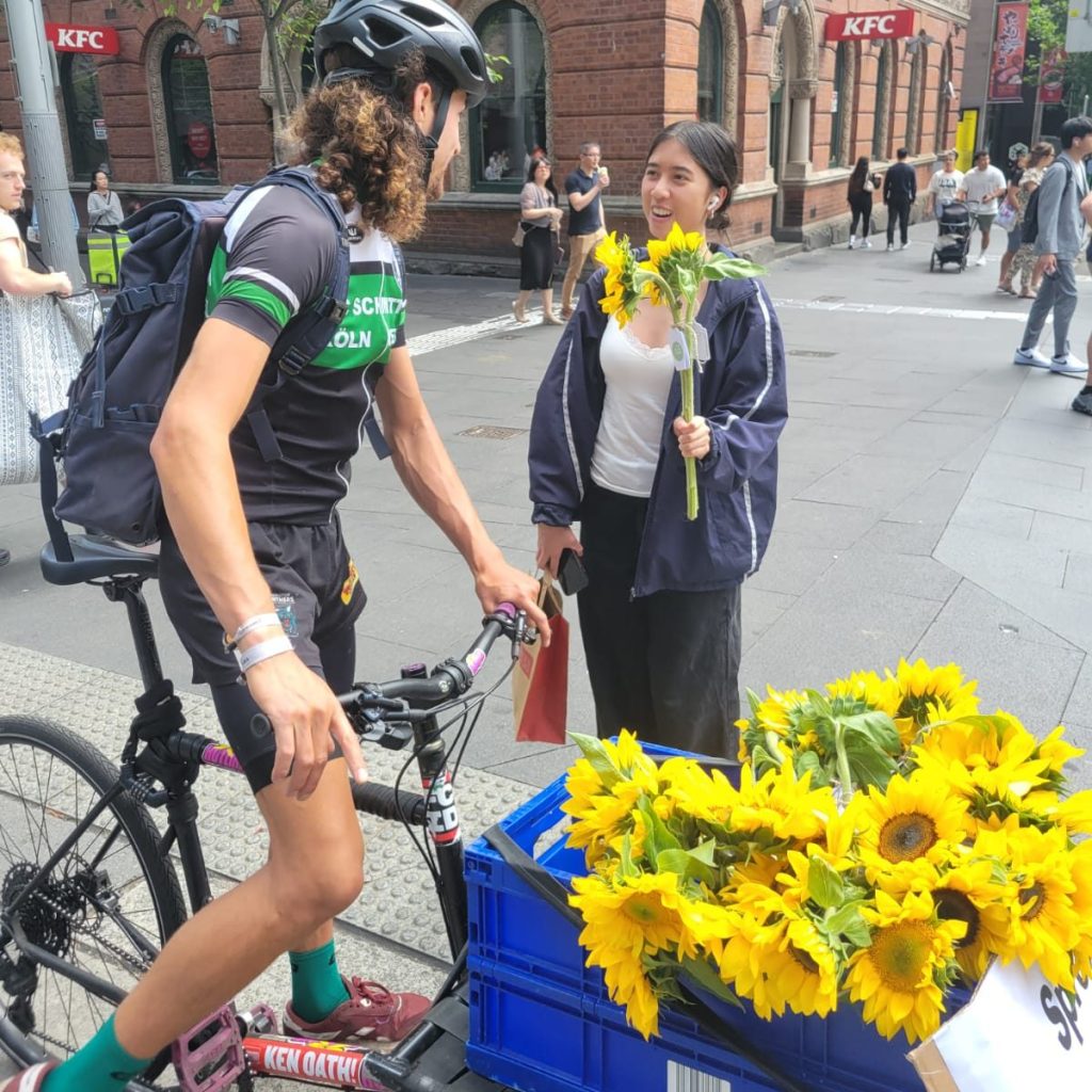 Cyclist gifting sunflowers to a passer-by in Sydney CBD