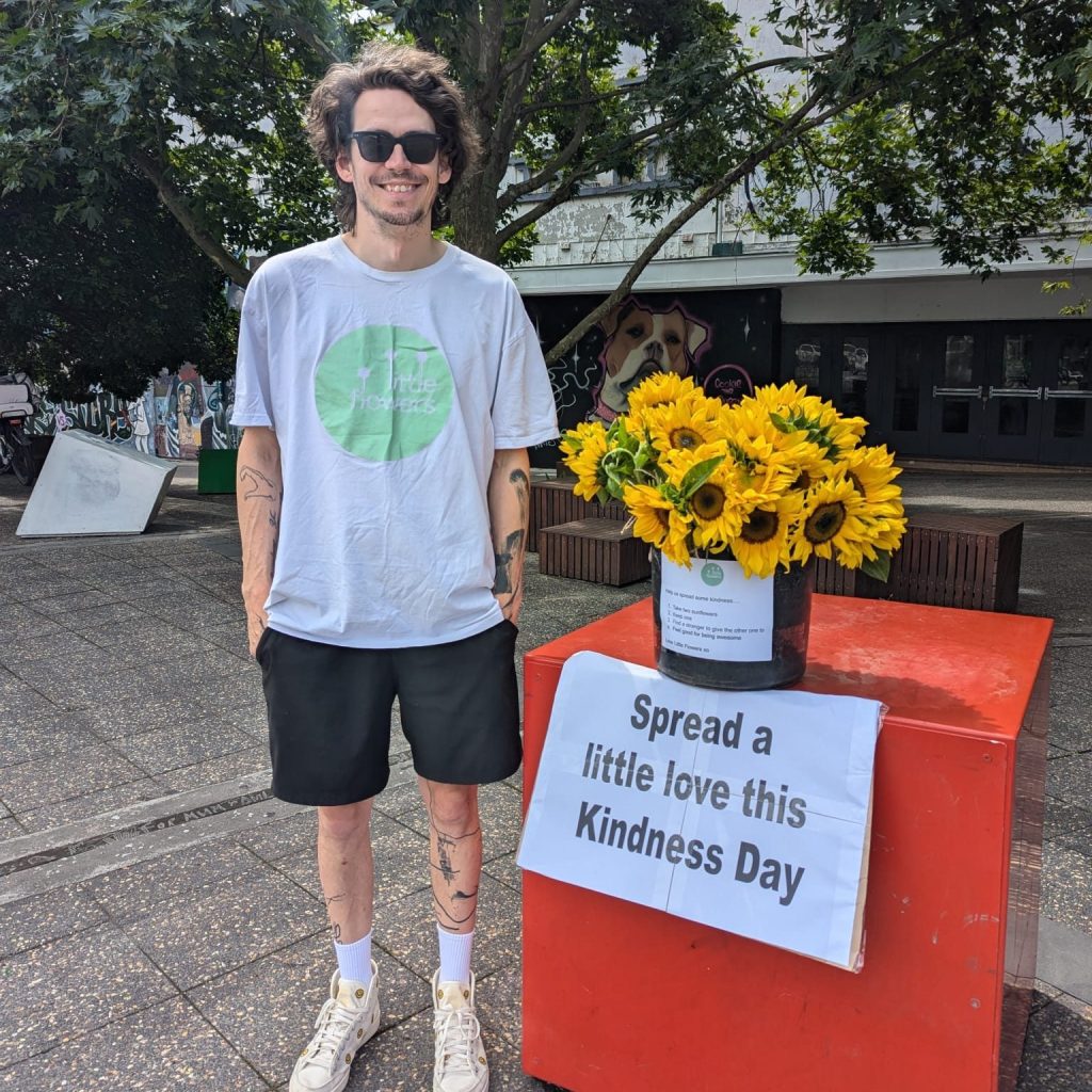 Little Flowers team member with a bucket of sunflowers and a Kindness Day sign in Newtown