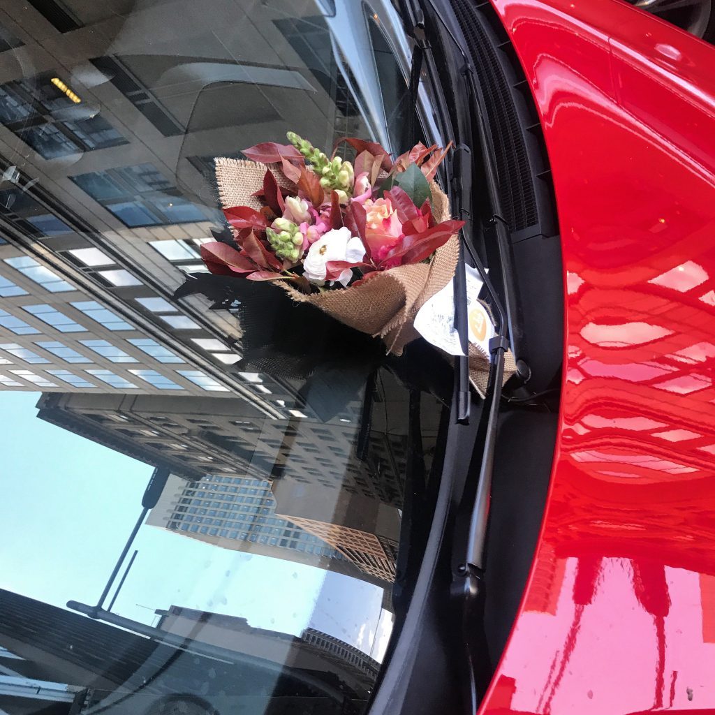 Small bouquet tucked under a car wiper beside a parking ticket in Sydney CBD